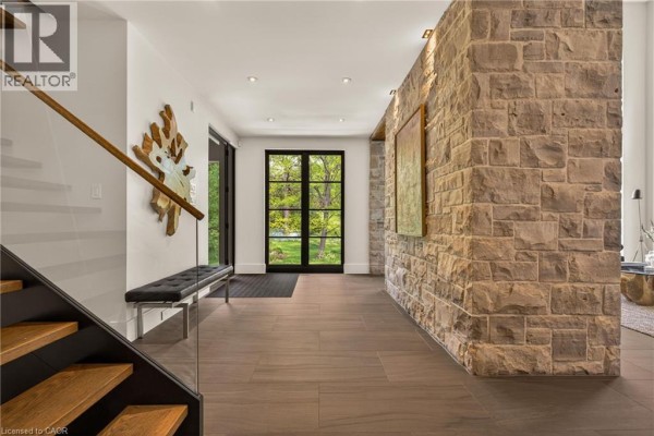 Interior foyer with a modern staircase, stone accent wall, and large double doors with a backyard view. - 981 Mineral Springs Road, Ancaster