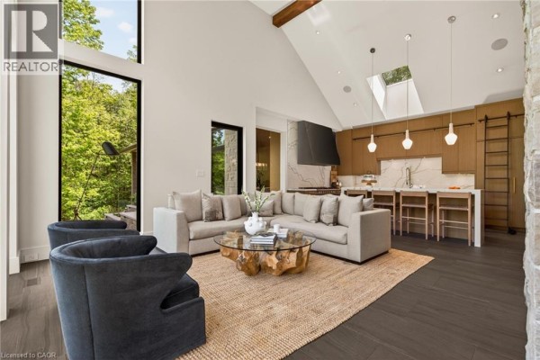 Spacious living room with a sectional sofa, unique coffee table, and an open-concept kitchen with island seating. - 981 Mineral Springs Road, Ancaster