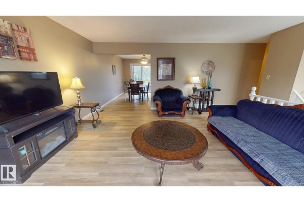 A galley kitchen with white cabinets and appliances adjacent to a carpeted room. - 9813 152 St Nw, Edmonton