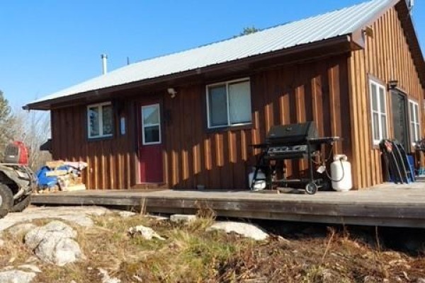 Side view of a brown wood-sided cottage with a metal roof and a gas grill. - 982 Musky Bay Road, St  Charles