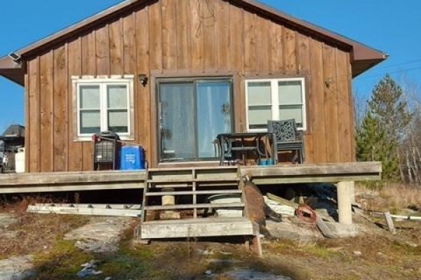 Front view of a wooden cottage with a sliding glass door and wooden deck stairs. - 982 Musky Bay Road, St  Charles
