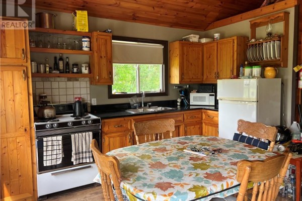Interior kitchen with pine cabinets, black countertops, a white stove, and a dining table. - 982 Musky Bay Road, St  Charles