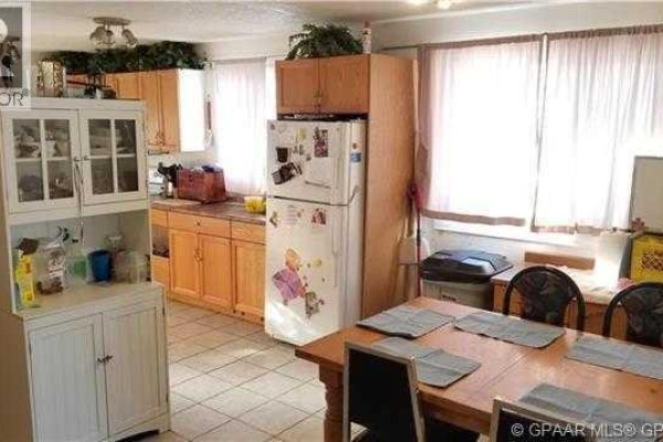 Kitchen area with light wood cabinets, white refrigerator, and dining table. - 9835 96 Avenue, Grande Prairie