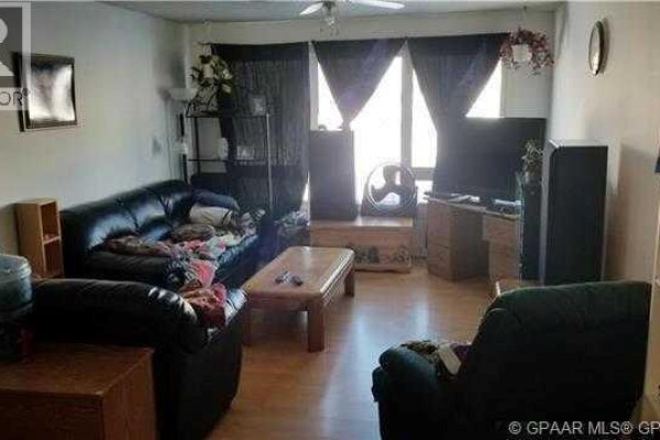Living room with dark leather sofas, a coffee table, and entertainment unit. - 9835 96 Avenue, Grande Prairie
