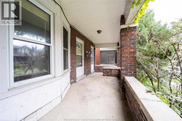 Covered front porch with brick pillars, concrete floor, and large windows. - 984 Windermere Road, Windsor