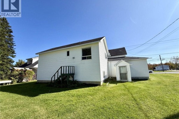 Side and back view of the white house with a wooden staircase and green lawn. - 985 Rue Louis G. Daigle, Tracadie