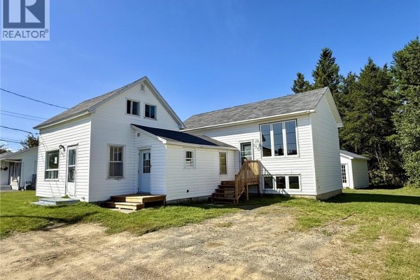 View of the white multi-unit house from the side with a driveway and green grass. - 985 Rue Louis G. Daigle, Tracadie