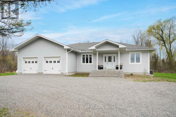 A light gray house with a double garage and a covered front entrance on a gravel driveway. - 986 South Gower Drive, North Grenville