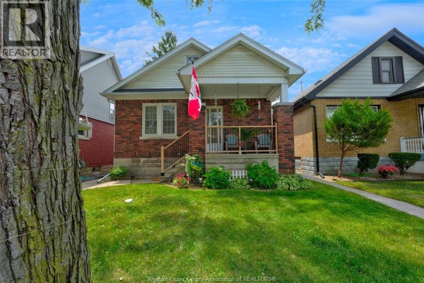 Front exterior of a red brick bungalow with a covered porch and lawn. - 987 Curry, Windsor