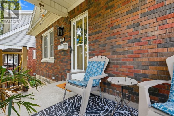 Close-up of a covered porch with seating and a red brick exterior wall. - 987 Curry, Windsor