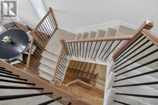 Overhead view of a U-shaped staircase with light carpet and wood railings. - 988 Beckton Heights, Ottawa