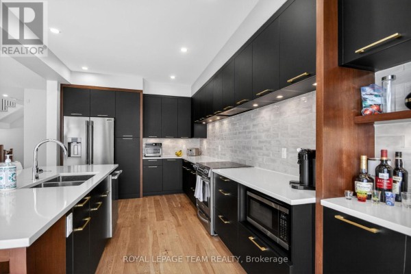 Contemporary kitchen with black cabinetry, white countertops, stainless steel appliances, and wood floor. - 988 Beckton Heights, Ottawa