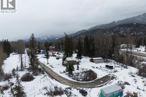 Overhead view of the property with snow-covered ground, trees, and distant mountains under an overcast sky. - 9898 Victoria Street, Hosmer