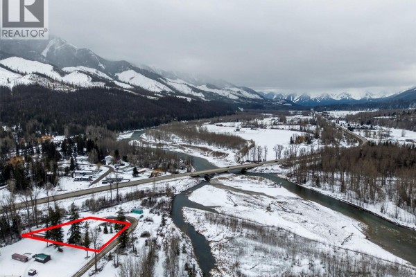 Wide aerial view of the property outlined in red, bordered by a river and surrounded by forested mountains. - 9898 Victoria Street, Hosmer