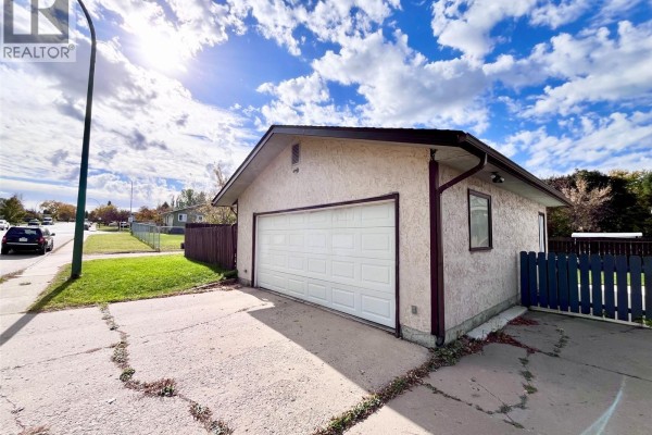 Exterior view of a detached single-car garage with a white overhead door and textured siding. - 99 Bowerman Crescent, Prince Albert