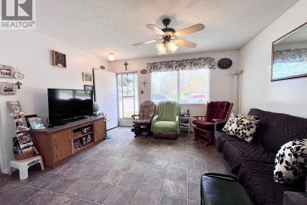 Living room with a dark couch, two rocking chairs, a television on a wooden stand, and tiled flooring. - 99 Bowerman Crescent, Prince Albert