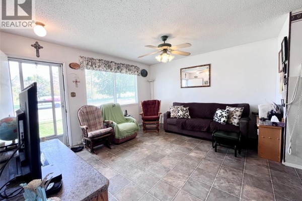 Living room with a couch, multiple chairs, a ceiling fan, a television, and large windows. - 99 Bowerman Crescent, Prince Albert