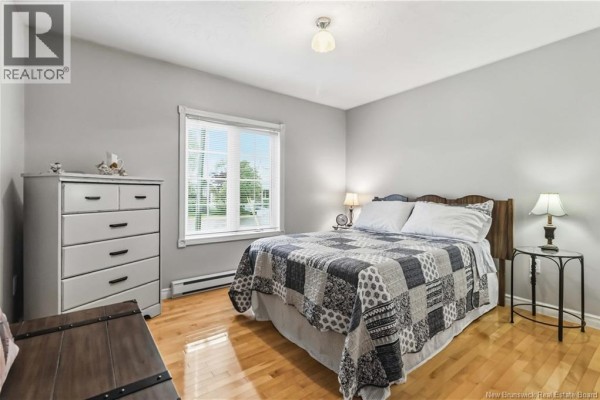 Bedroom with light grey walls, a queen-size bed, a grey patchwork quilt, and a white dresser. - 99 Fairview Knoll Drive, Moncton