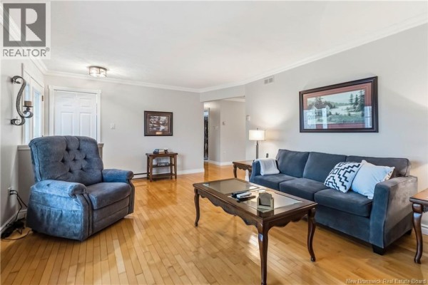 Living room with light grey walls, a dark blue sofa, a tufted grey recliner, and wooden floors. - 99 Fairview Knoll Drive, Moncton
