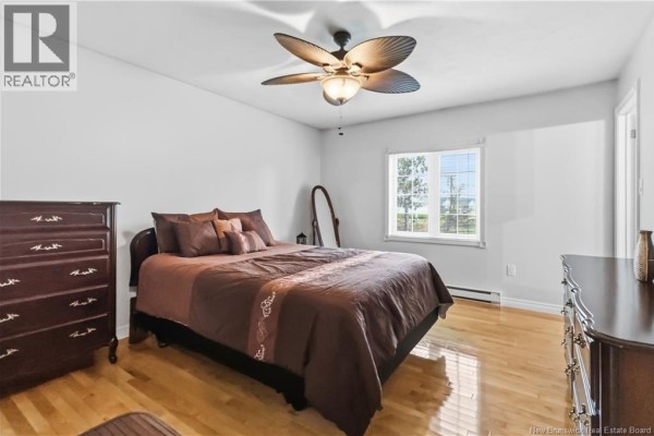 Bedroom with light grey walls, a queen-size bed with brown bedding, and two dark wood dressers. - 99 Fairview Knoll Drive, Moncton