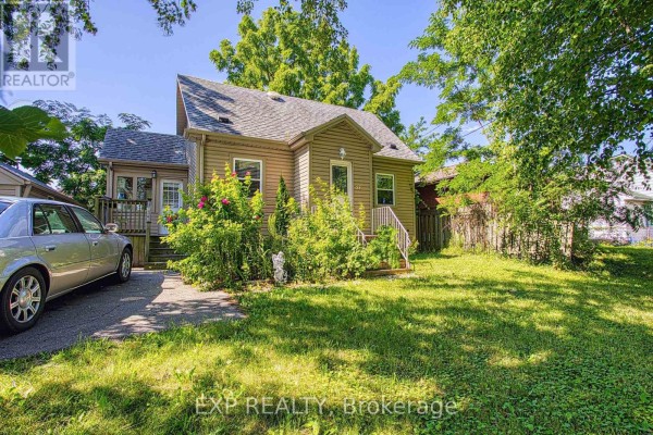 A different angle of the beige house with brown siding, featuring green shrubs and a driveway with a silver sedan. - 99 Mohawk Road W, Hamilton