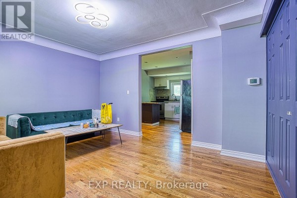 A living room with light purple walls, hardwood floors, a green sofa, and an opening to the kitchen. - 99 Mohawk Road W, Hamilton