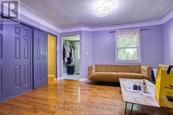A living room with light purple walls, hardwood floors, a gold sofa, a coffee table, and purple bi-fold doors. - 99 Mohawk Road W, Hamilton