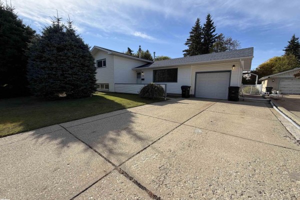 Front exterior of a white house with a concrete driveway and mature evergreen trees. - 99 Pine St, Sherwood Park