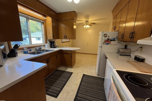 Kitchen with wood cabinets, white countertops, double sink, and view of dining area. - 99 Pine St, Sherwood Park