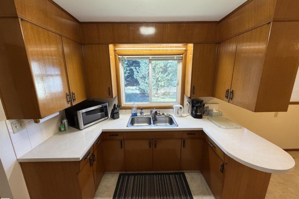 U-shaped kitchen with wood cabinets, white countertops, double sink, and backyard view. - 99 Pine St, Sherwood Park