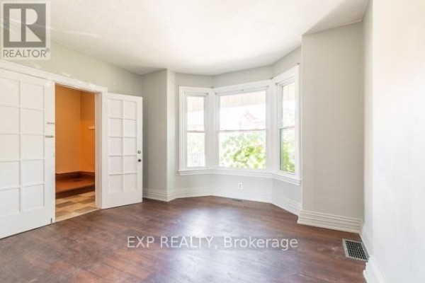 Living room with a bay window, white double doors, and dark wood floors. - 99 Sanford Avenue N, Hamilton