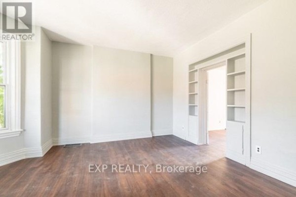 Empty room with light grey walls, dark wood floors, and built-in shelving. - 99 Sanford Avenue N, Hamilton