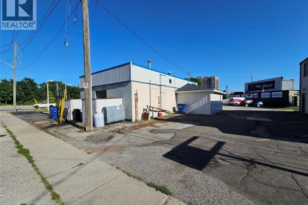 Back view of a commercial building with white siding, gray roof, and storage tanks outside. - 99 Thames Street, Chatham