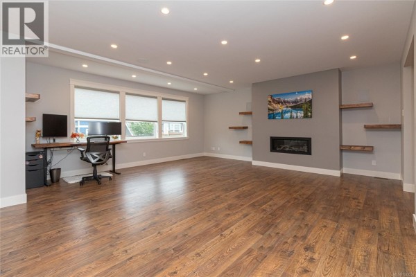 Open-concept living space with hardwood floors connecting to a kitchen with an island and bar stools. - 990 Ariane Gdns, Langford