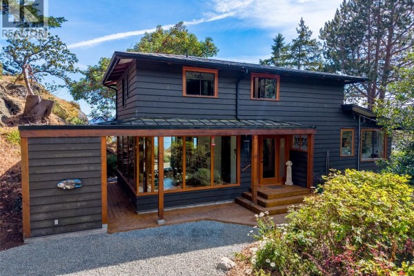 Front exterior of a dark siding house with covered porch and waterfront view. - 9919 Southlands Dr, Pender Island