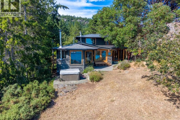 Dark grey house with large windows and a hot tub on a dry, grassy slope. - 9919 Southlands Drive, Pender Island
