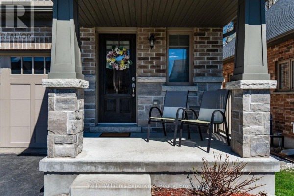 Front porch of a townhouse with two chairs, a dark door, and stone pillar accents. - 992 Cook Drive, Midland