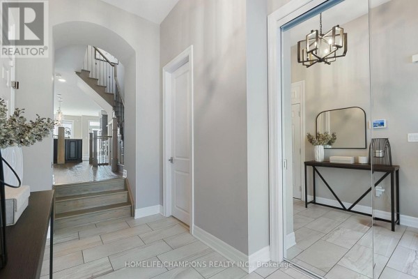 Interior entryway with light grey walls, beige tiled floor, a staircase, and a console table with a mirror. - 993 Dragonfly Avenue, Pickering