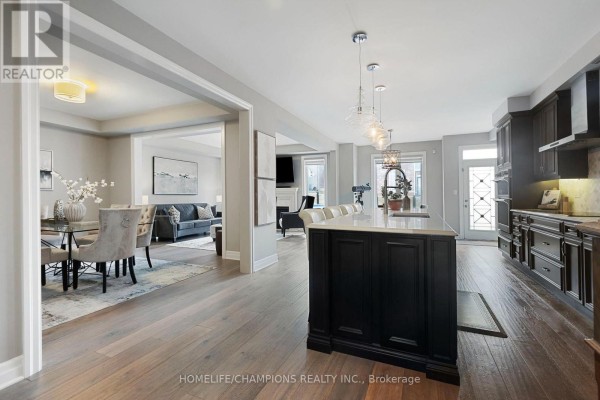 Open concept living and dining area with hardwood floors, fireplace, and a large kitchen island with bar stools. - 993 Dragonfly Avenue, Pickering