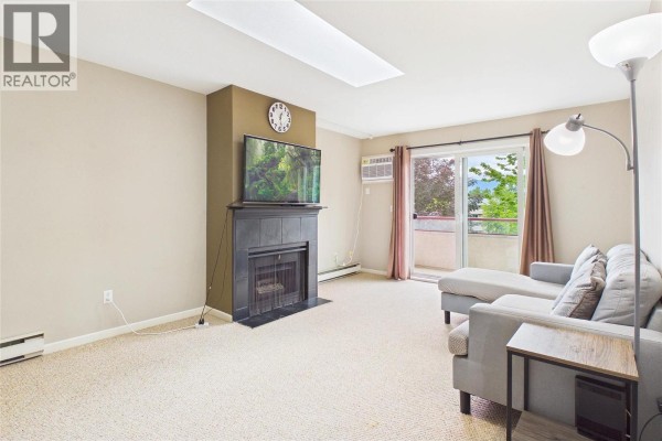 Living room with a grey sectional sofa, fireplace, television, and sliding glass door. - 993 Klo Road Unit# 303, Kelowna