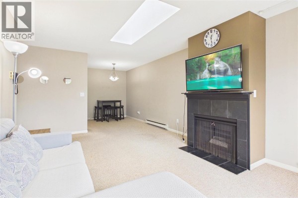 Living room with a grey sectional sofa, fireplace, television, and dining area with table. - 993 Klo Road Unit# 303, Kelowna