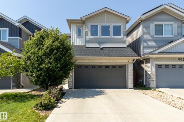 Front exterior view of a two-story duplex with a double garage and light gray siding. - 9932 223 St Nw, Edmonton