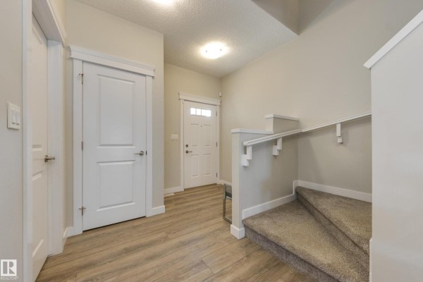 Interior entryway with a white front door, light wood laminate flooring, and carpeted stairs. - 9932 223 St Nw, Edmonton