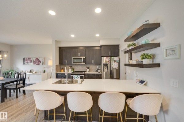 Modern kitchen with dark cabinets, stainless steel appliances, and a large white quartz island. - 9932 223 St Nw, Edmonton