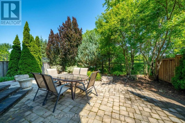 Paved backyard patio with a glass-top dining table and four chairs surrounded by trees. - 995 Nellie Little Crescent, Newmarket