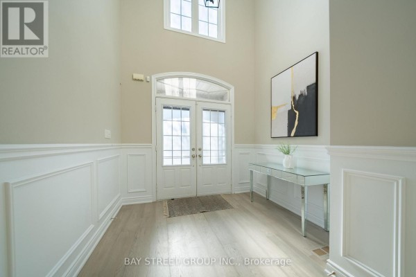 Foyer with double doors, light wood floors, wainscoting, and a mirrored console table. - 995 Nellie Little Crescent, Newmarket