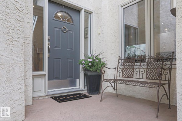 Grey front door with decorative metal bench and potted flowers. - 995 Ogilvie Bv Nw, Edmonton