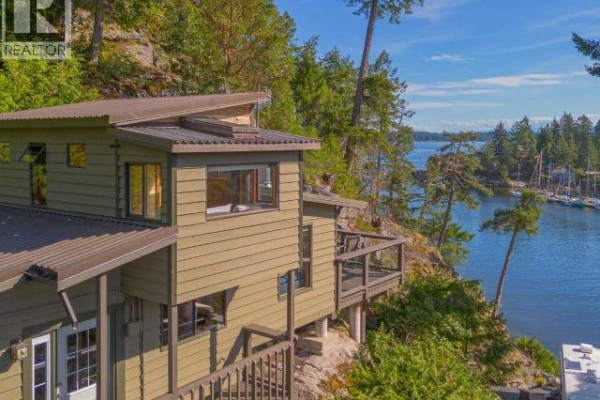 Side view of a house with green siding and a metal roof, built on a rocky slope by the water. - 9951 Finn Bay Rd, Powell River