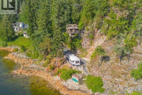 Aerial view of a house on a steep, wooded lot with an RV parked on the driveway near the water. - 9951 Finn Bay Rd, Powell River