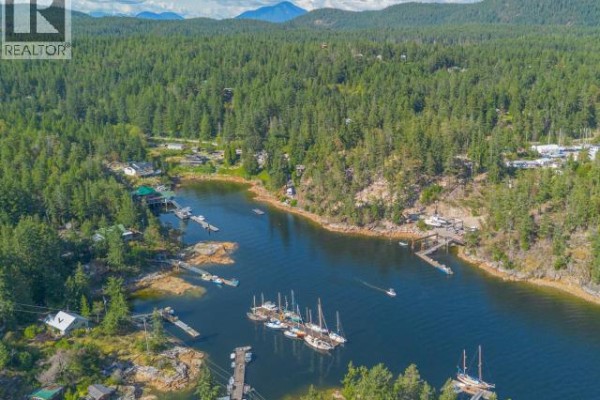 Aerial view of a natural harbor with numerous sailboats docked and homes nestled amongst dense trees. - 9951 Finn Bay Rd, Powell River